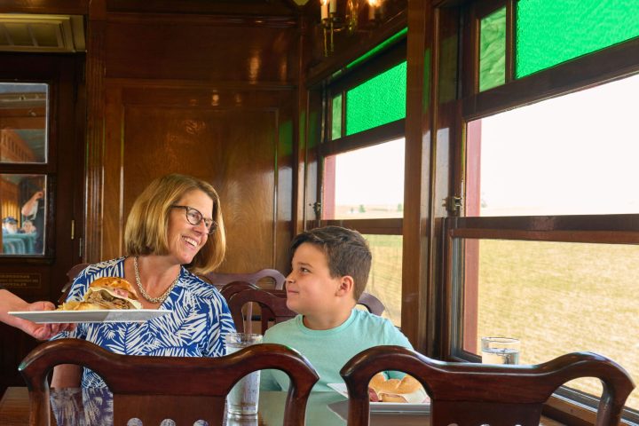 A mom and her son sitting at a dining table on the train.