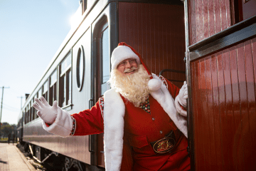 Santa leaning outside the train car while smiling and waving.