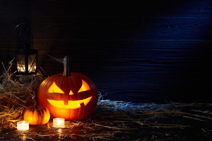 A lit jack o lantern sitting inside a dark barn with candles around it.