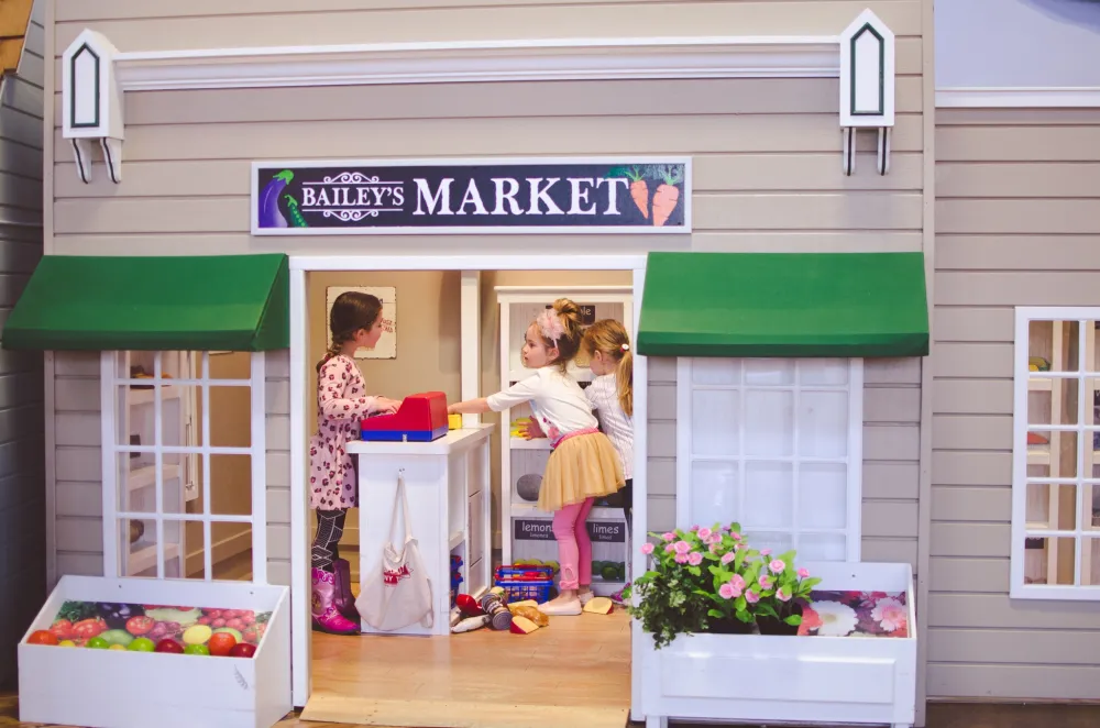 Tiny Town's miniature indoor playhouses with girls playing inside a market.
