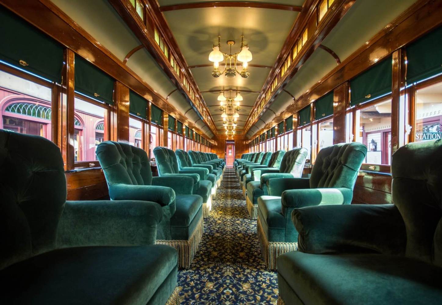 An upholstered first-class train car with lines of armchairs.
