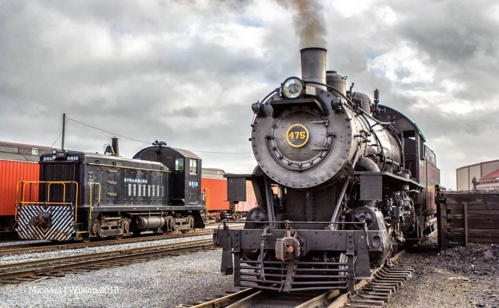 Steam engine 475 is sitting on a train track outside of Strasburg Rail Road train station.