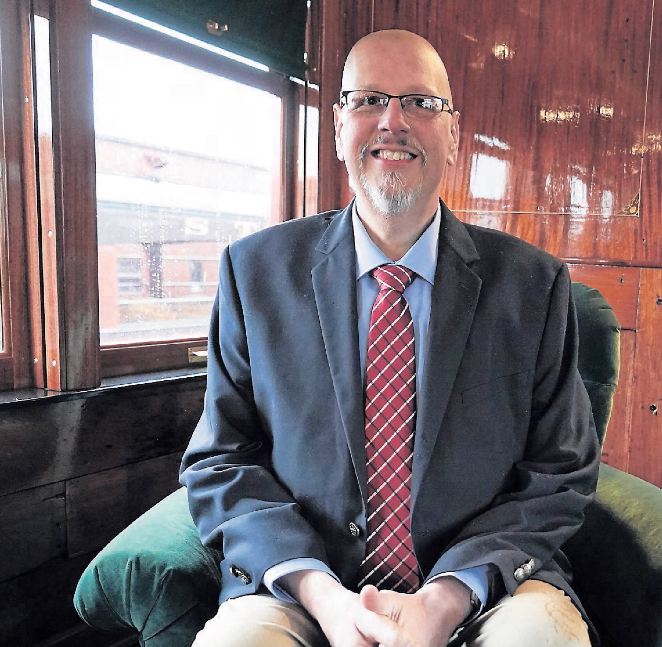 Craig R. Lefever wearing a suit and tie sitting in front of a window