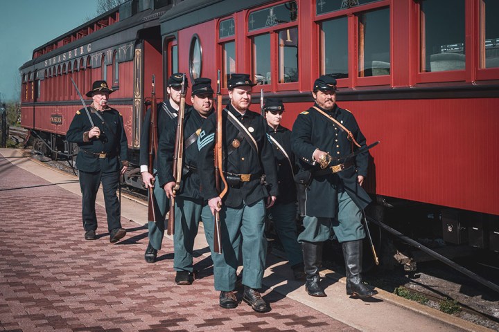 A group of people in uniform standing next to the train holding their rifles.