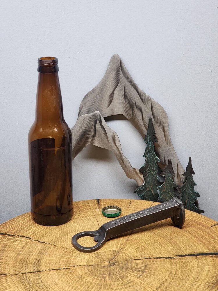 Railroad spike bottle opener sitting next to an empty beer bottle.