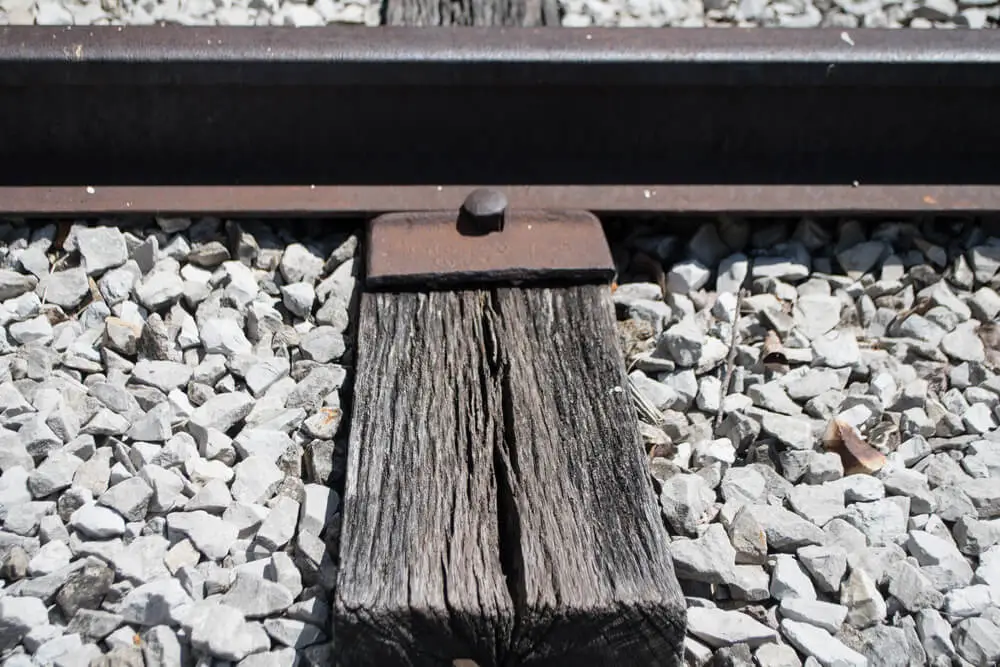 Close up of a wooden railroad tie secured in place by a railroad spike.